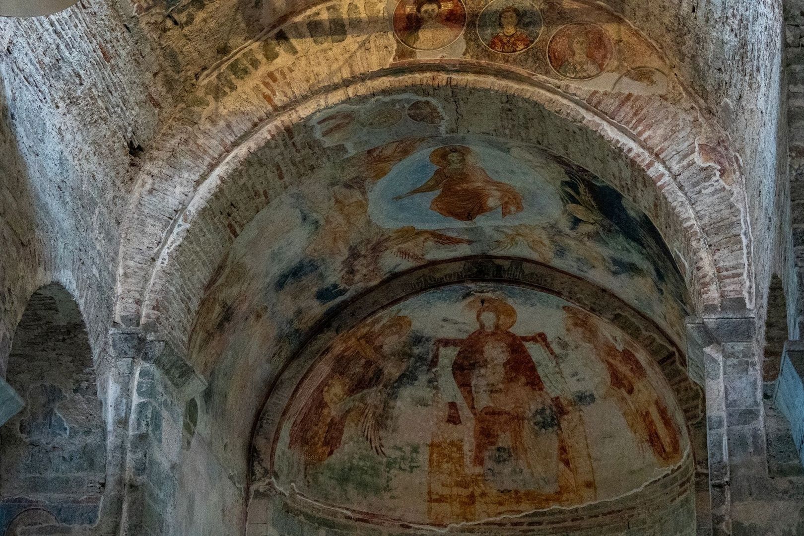 Weathered medieval frescoes covering a vaulted stone church apse