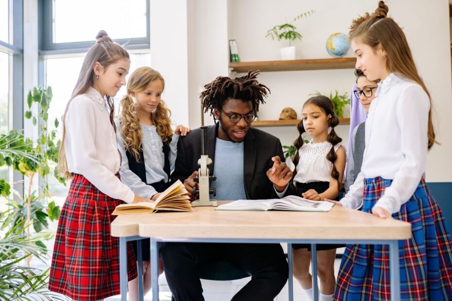 Teacher and diverse schoolchildren gather around books and a microscope